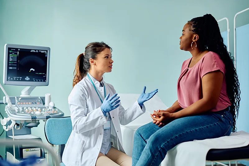 A doctor speaks with a female patient who is sitting on the examination bed