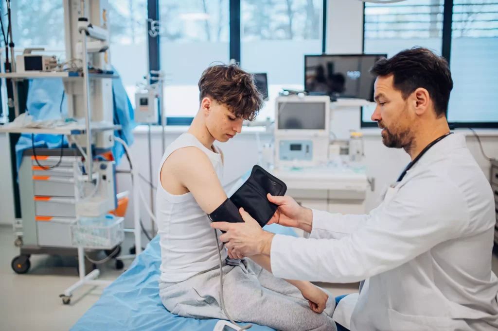 Teen boy undergoing medical checkup with doctor in hospital room.