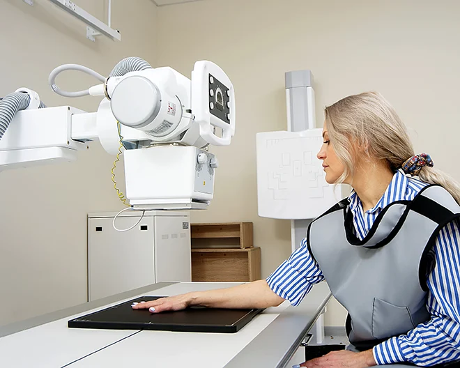 A woman sits still while receiving an xray of her wrist and arm